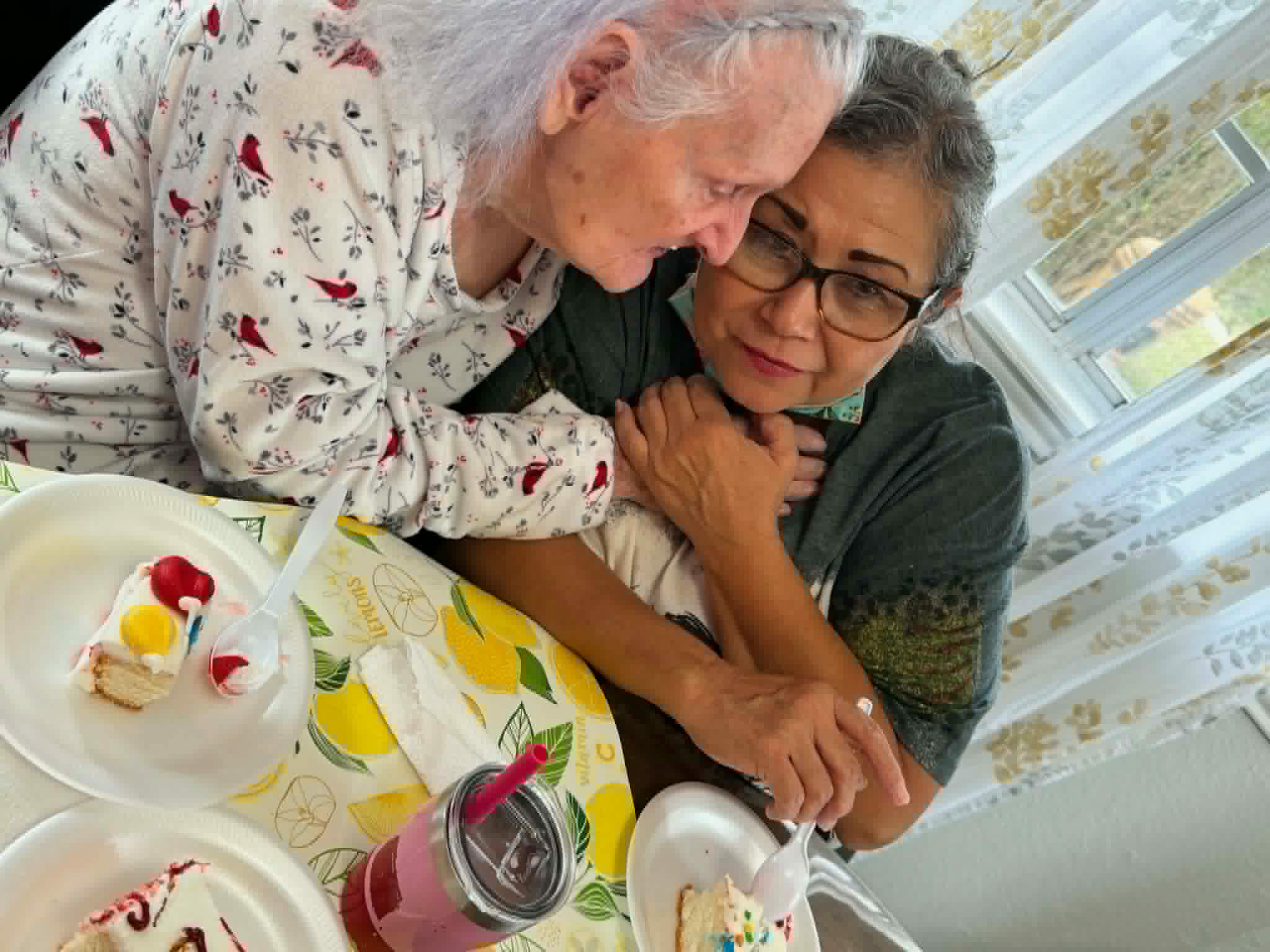 A caregiver comforting a resident with a hug while sharing birthday cake